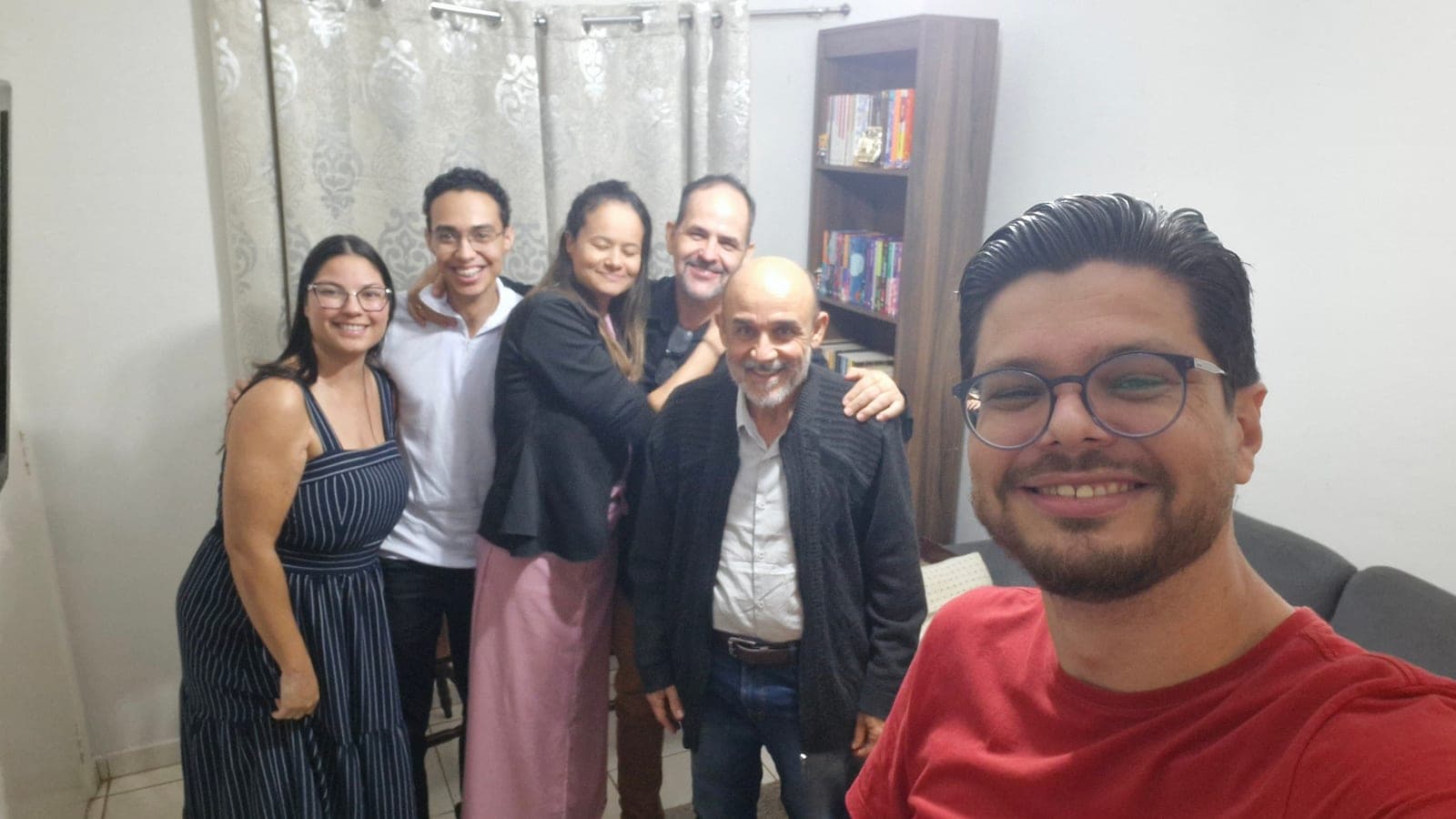 Seis pessoas abraçadas na sala de casa, sorrindo no fim do segundo encontro